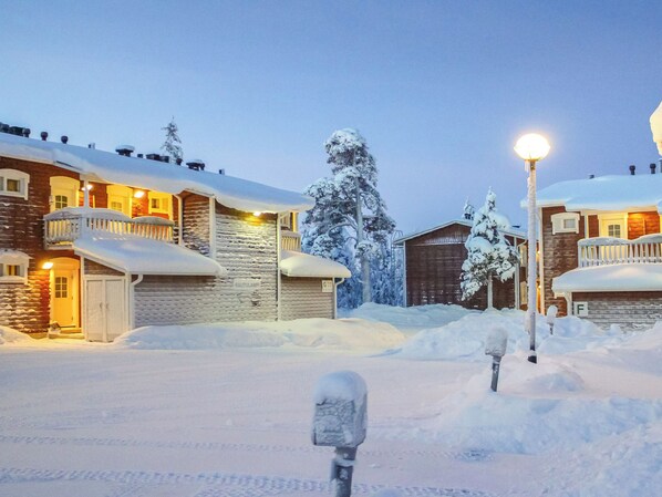 A snow-covered residential area with houses, a wooden cabin, and a street lamp.