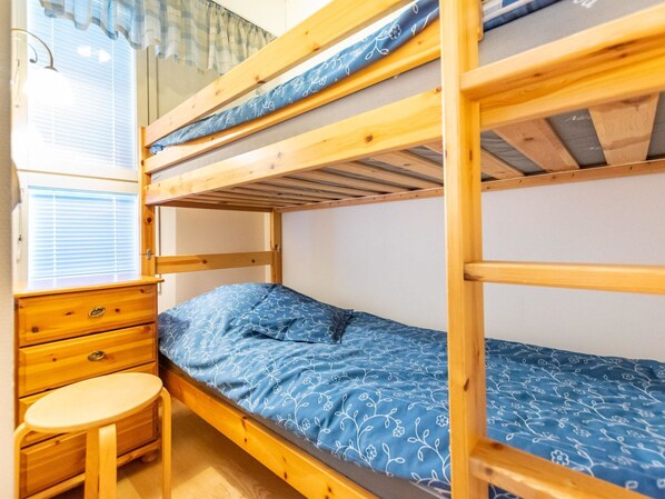 Habitación con literas, un escritorio de madera y una silla, una ventana con persianas y una colcha estampada.