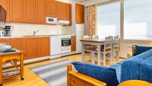 A modern kitchen with wooden cabinets, a dining area with a table and chairs, and a blue sofa.
