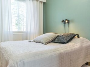 Une chambre à coucher avec un lit, une fenêtre avec des rideaux et une lampe fixée au mur.