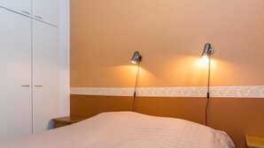 Een slaapkamer met een bed, twee bedlampen, een kledingkast en een decoratieve rand aan de muur.