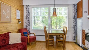 Een gezellige woonkamer met een rode bank, een houten eettafel en een keuken met een koelkast en fornuis.
