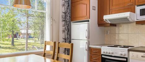Ett kök med träskåp, ett vitt kylskåp, en spis och ett matbord med stolar.