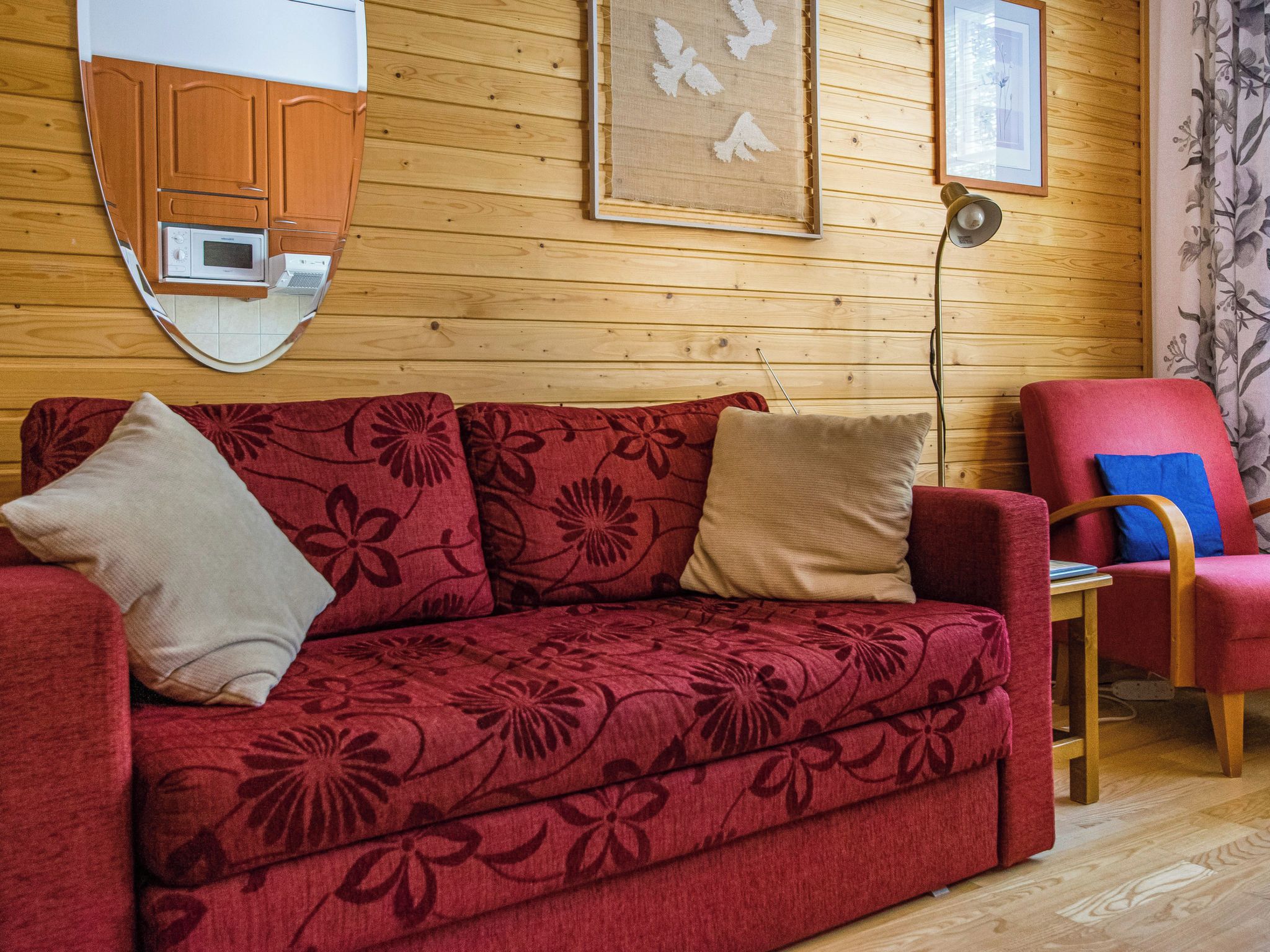 Een rode bank met bloemenstof, een houten wand, een lijst met een afbeelding en een rode fauteuil.