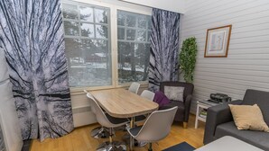 Un salon moderne avec une table à manger en bois, deux chaises, un canapé gris et une petite table d’appoint sur laquelle se trouve une radio.