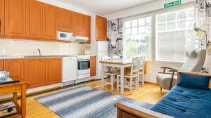 A compact kitchen with wooden cabinets, a microwave, and a dining area with a table and chairs. - Outapailakka j 9 by Interhome (Inari)