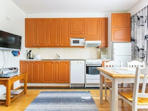 Una cocina con armarios de madera, microondas, lavavajillas, horno y una mesa de comedor con sillas.