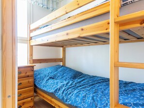 Ein Stockbett mit Holzrahmen, ein Einzelbett darunter und eine Holzkommode mit Schubladen.