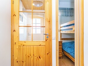 Una puerta de madera con un ventanal, una lámpara arriba y una litera con un colchón azul visible desde el interior.