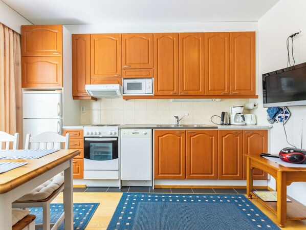 A compact kitchen with wooden cabinets, a microwave, a stove, a dishwasher, and a TV on the wall.
