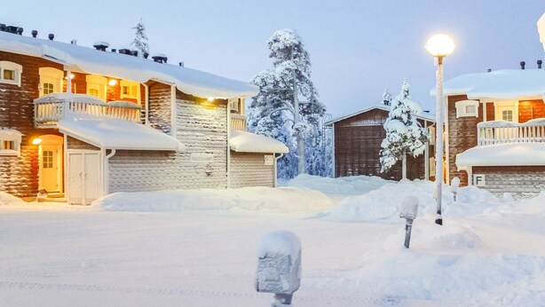 A snow-covered village with wooden buildings, a wooden barn, and a street lamp.