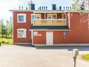 Ein rotes Gebäude mit Balkon und einer Tür, auf der 'OUTPAILAKKA' steht, sowie einem blauen Behindertenschild.