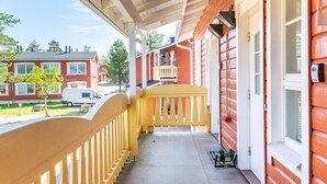 A covered porch with a yellow railing, a red brick building, and a white vehicle parked outside.