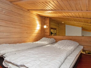 Een kamer met twee bedden, houten wanden, een plafond met houten balken en een wandlamp.