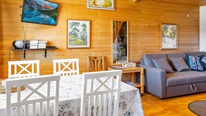 Ein gemütliches Zimmer mit Holzwänden, einem Esstisch mit Stühlen, einem grauen Sofa und gerahmten Bildern an den Wänden.