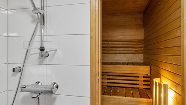 Eine Sauna mit einer Holzbank und einem Duschbereich mit Chromarmaturen.