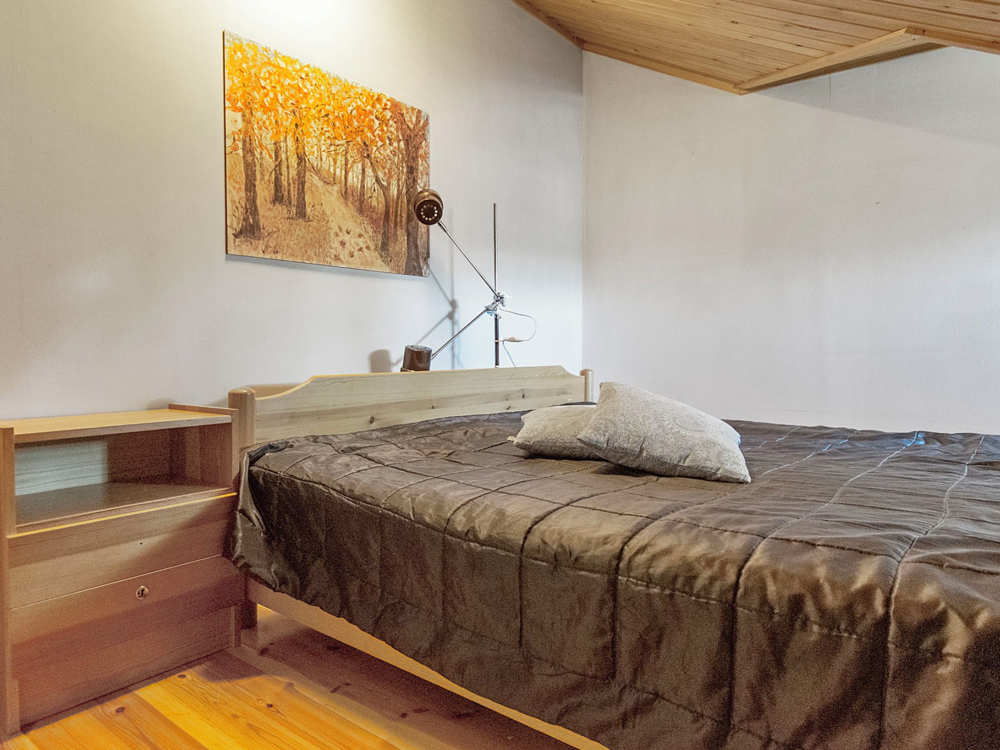 Une chambre à coucher comprenant un lit, une table de chevet en bois, un bureau, une chaise et une lampe fixée au mur.