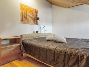 Ein Schlafzimmer mit einem Bett, einem Holznachttisch, einem Schreibtisch, einem Sessel und einer Wandlampe.