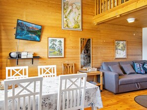 A wooden interior with a dining table, chairs, a sofa, and artwork on the walls.