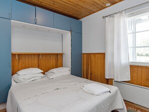 Una habitación con cama, cabecera de madera, armarios azules y una ventana con cortinas.
