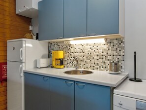 Una cocina compacta con un refrigerador blanco, una cafetera y un lavamanos.