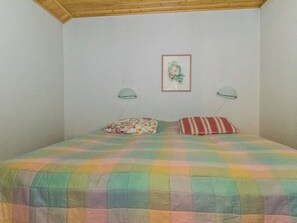 Une chambre avec une couvre-lit à carreaux, deux oreillers, une œuvre d’art florale encadrée accrochée au mur et deux lampes fixées au mur.