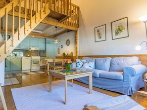 Un salon avec un canapé bleu, un escalier en bois et une cuisine à l’arrière-plan.
