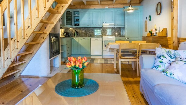 Una escalera de madera conduce a una cocina con armarios azul turquesa, un comedor con una mesa y sillas, y una sala de estar con un sofá.