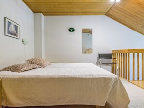 Een slaapkamer met een bed, een wandklok, een spiegel en een houten leuning.