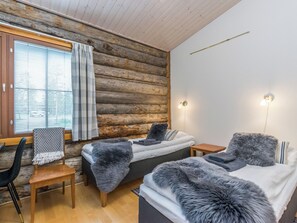 A cabin-style room with a wooden log wall, a bed with a fur throw, a chair, and a small table.