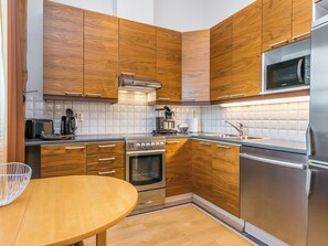 A modern kitchen with wooden cabinets, stainless steel appliances, and a round wooden table.