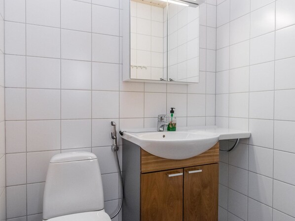 Une salle de bain avec des carreaux blancs, des toilettes blanches, un meuble en bois et un miroir au-dessus du lavabo.