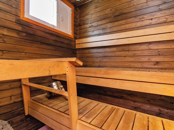 A wooden sauna with benches and a metal container on the floor.