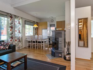 En moderne stue med sofa, spisebord med stole, pejs og et køkkenområde med skabe og et køleskab.