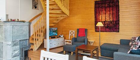 A cozy living room with a fireplace, wooden walls, a staircase, and a large tapestry.