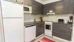 Een kleine keuken met een koelkast, magnetron, vaatwasser, fornuis en kastjes.