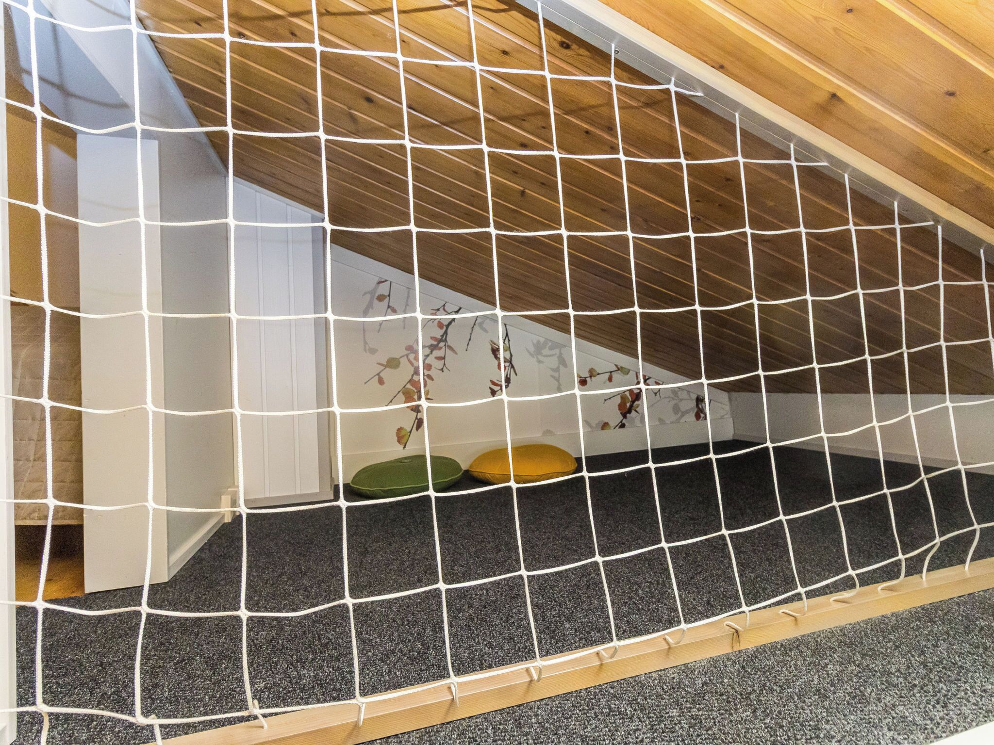 A room with a sloped ceiling, a wooden floor, and a netted play area.