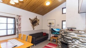 Een gezellige woonkamer met een stenen open haard, houten plafond en een groot raam met gordijnen.