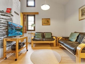 Una sala de estar acogedora con televisor, sofá, sillón, alfombra y una ventana con cortinas.