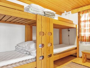 Een slaapkamer met stapelbedden, een houten plafond, een tafeltje en een raam met gordijnen.