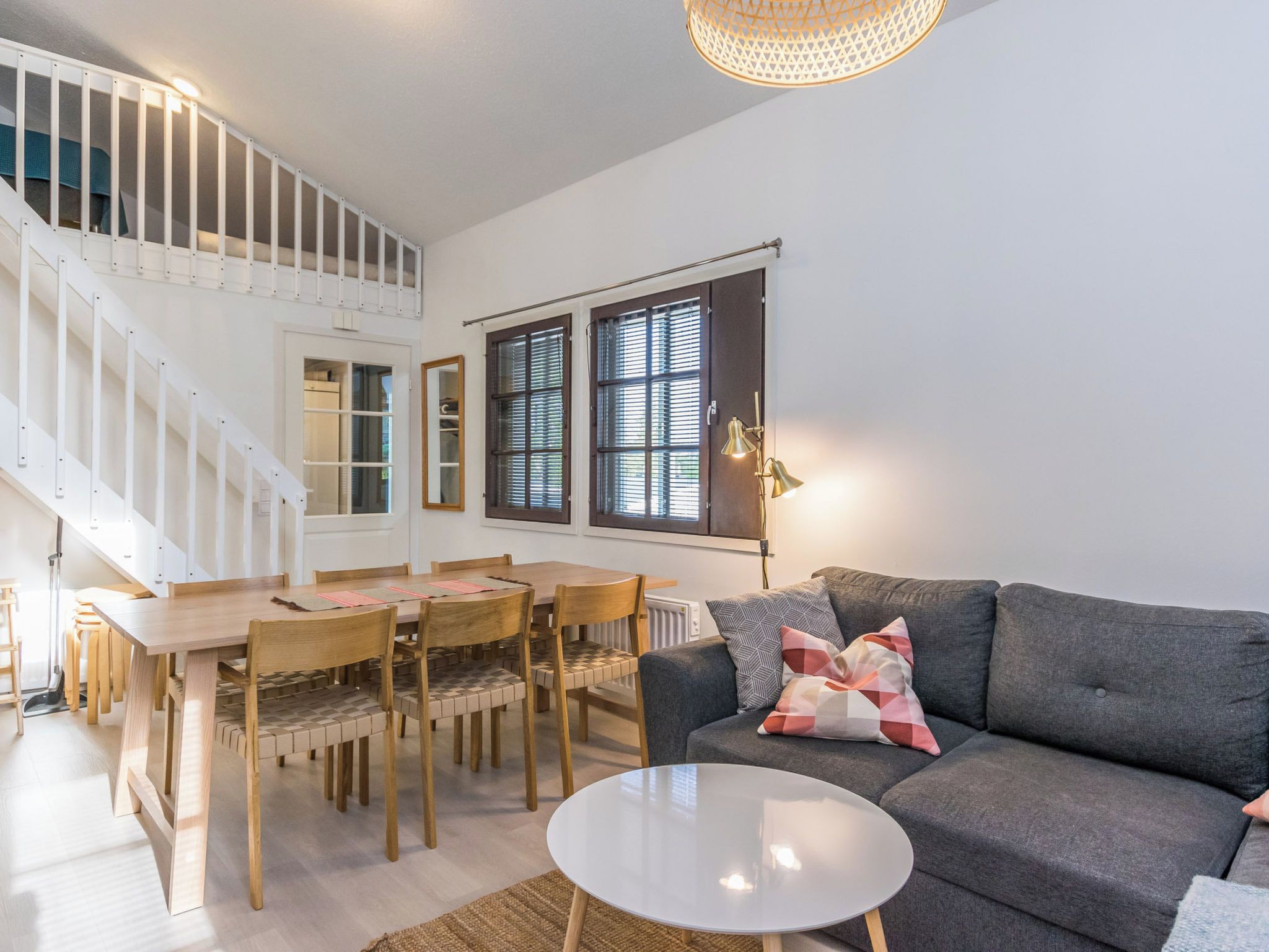 Un salon moderne avec un escalier, un coin repas et un canapé gris agrémenté de coussins.