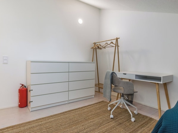 Een kamer met een witte garderobe, een bureau met stoel, een kledingrek en een rode brandblusser.