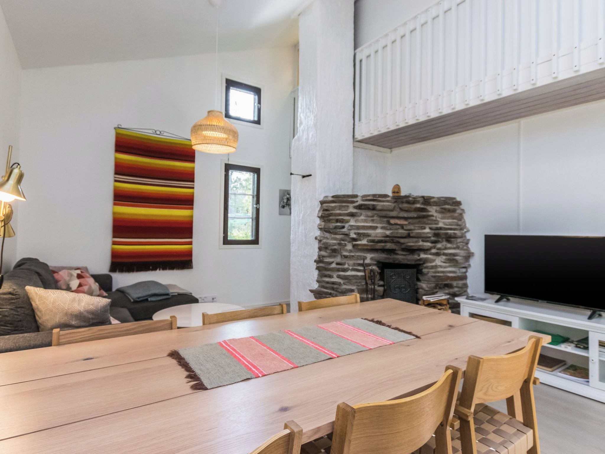 A modern living room with a stone fireplace, a dining area with a wooden table and chairs, a sofa, and a television.