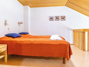 Een slaapkamer met een bed, kussens, een nachtkastje, een lamp en een houten leuning.