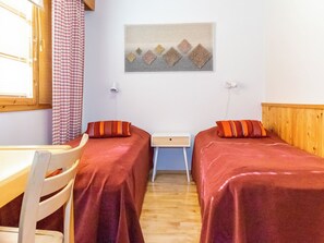 Una habitación con dos camas, una mesita, una silla y un cuadro en la pared.