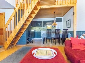A room with a wooden staircase, a dining area with chairs and a table, and a red sofa.