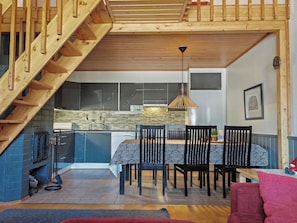 Cocina moderna con comedor, escalera de madera y lámpara colgante.