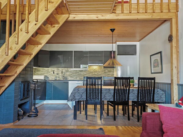 A modern kitchen with a dining area, wooden staircase, and a pendant light.