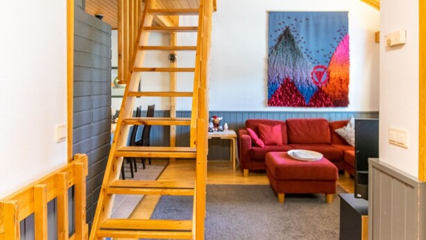 Un escalier en bois mène à une mezzanine où se trouvent un canapé rouge et un tableau abstrait aux couleurs vives.