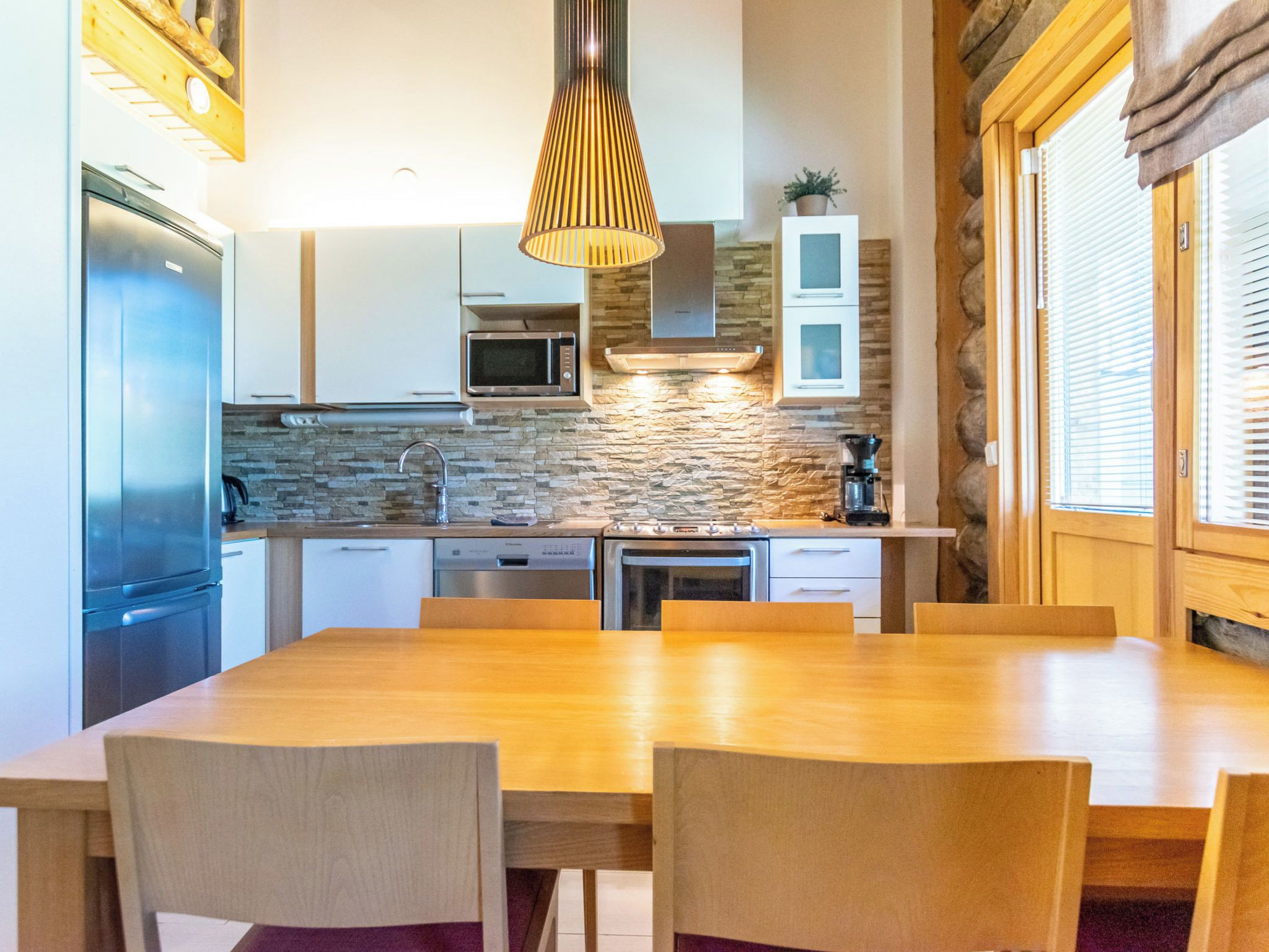 Une cuisine moderne avec une table et des chaises en bois, un four à micro-ondes encastré et un pare-feu en pierre.